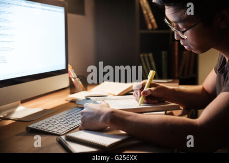 Serious asian young man studying with books and computer in dark room at home Stock Photo