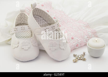 Pair of white baby shoes on embroidered christening white dress, cross and candle Stock Photo