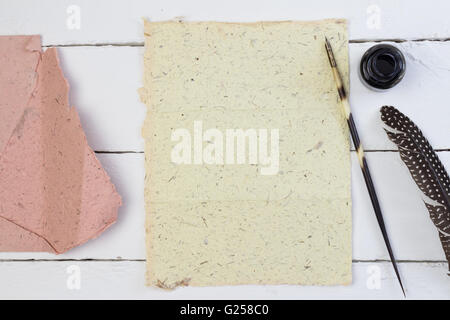 Close up of hand made blank piece of elephant dung paper with quill pen, ink pot and feather on white wood table outside Stock Photo