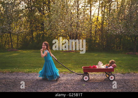Smiling Girl in dress pulling wagon with doll and bear Stock Photo