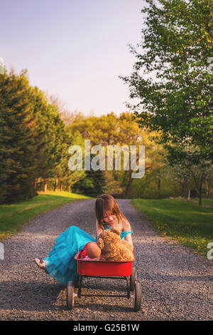 Girl sitting in wagon with doll and teddy bear Stock Photo