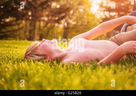 Boy lying on grass in garden laughing Stock Photo