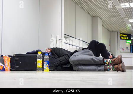 Two young men sleeping on airport terminal floor at Manchester Airport. UK Stock Photo