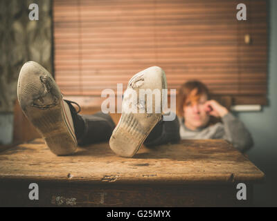 A young woman wearing worn out shoes is resting her feet on a table at home Stock Photo