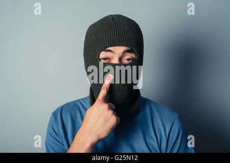 A stupid man wearing a balaclava is trying to pick his nose Stock Photo
