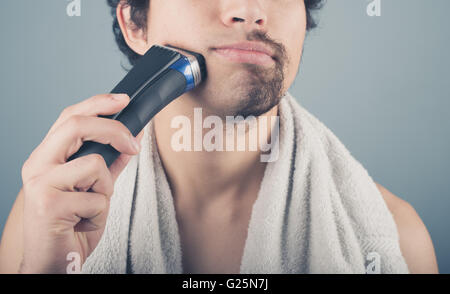 A young man is shaving off half of his beard Stock Photo