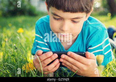 Child lying on the grass in summer suth mobile phone Stock Photo