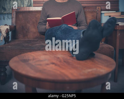 A young man is relaxing on a sofa at home and is reading a book Stock Photo