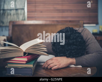 A tired student is asleep with his head on a coffee table surrounded by books Stock Photo
