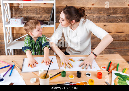 Cheerful little boy and his mother making prints of painted hands in colorful paint on the paper Stock Photo