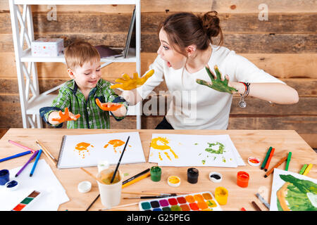 Smiling amazed young mother and her little son making prints by hands and paints on the paper Stock Photo