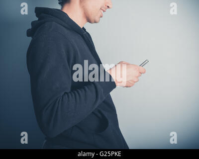 A young man wearing a hooded top is using his smartphone Stock Photo