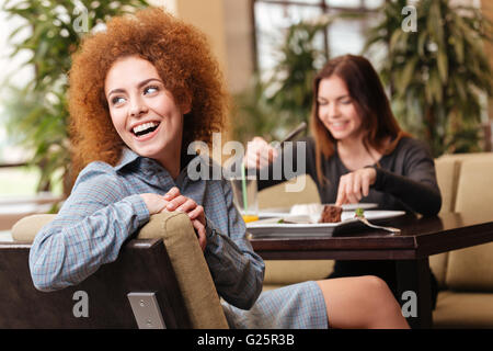 Two cheerful beautiful young women sitting in cafe and laughing together Stock Photo