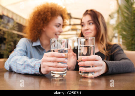 Two smiling charming young women drinking water at the table in cafe Stock Photo