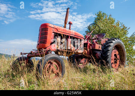 Old red rusty tractor in a field Stock Photo