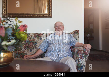 Indoor shot of happy senior man sitting relaxed on a couch at old age home. He is looking at camera and smiling. Stock Photo