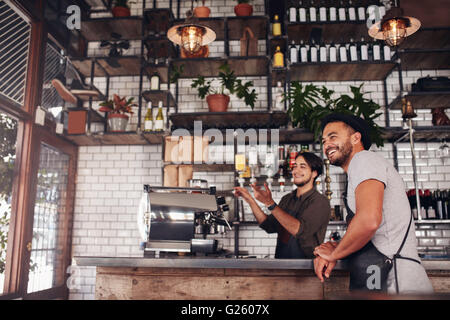 Coffee shop workers standing at the counter looking outside the cafe and smiling. Stock Photo