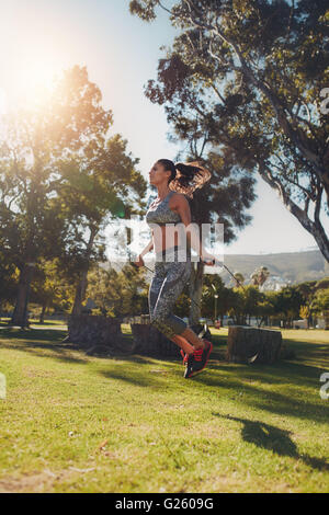 Full length outdoor shot of young woman skipping with a jump rope outdoors. Woman doing fitness training in a park on a sunny da Stock Photo