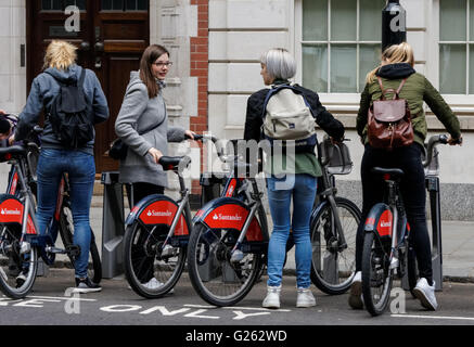 Young girls parking bikes at Santander Cycles Hire docking station in Westminster, London England United Kingdom UK Stock Photo