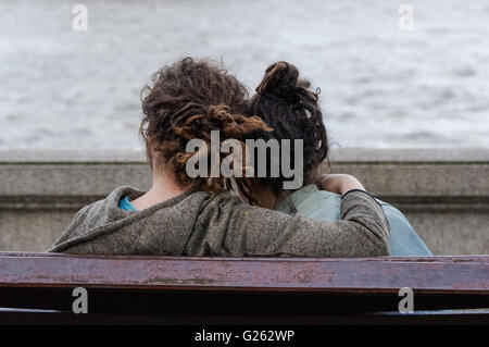 Young couple sitting on a bench on the bank of river, London England United Kingdom UK Stock Photo