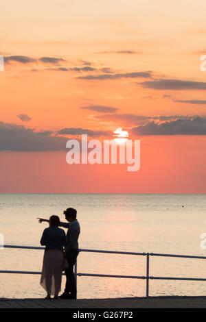 Aberystwyth, Wales, UK. 24th May, 2016.  UK weather:  A young couple talking a evening walk on the promenade are silhouetted against a spectacular sunset over Cardigan Bay in Aberystwyth on the west Wales coast UK.     photo Credit:  Keith Morris / Alamy Live News Stock Photo