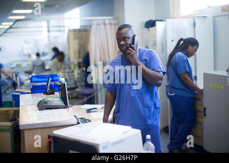 Hospital nurse at a workstation in a ward answering enquiries and checking medical records Stock Photo