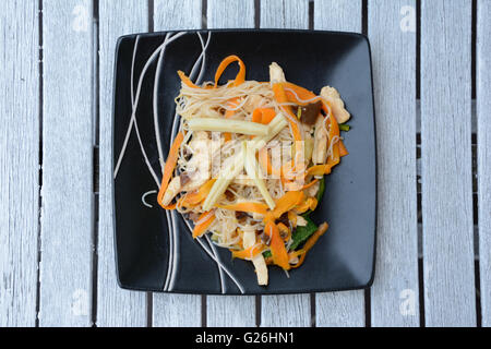 Dish consisting of chinese rice noodles and cooked vegetables on black plate. Stock Photo