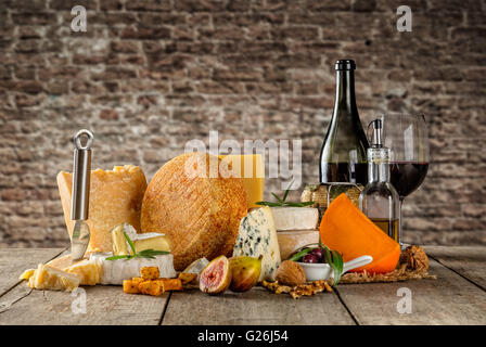 Various types of cheese, glass and bottle of red wine placed on wooden table, copyspace for text. brick wall on background Stock Photo