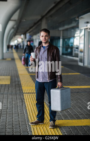 Young attractive man drinking coffee on his way near the airport terminal looking to the camera Stock Photo