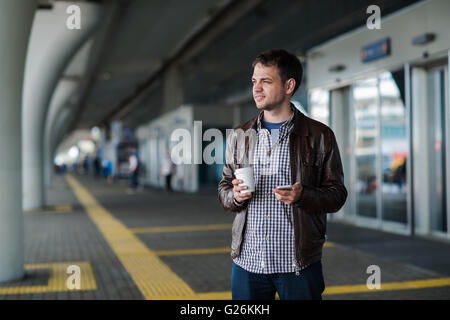 Man with cellphone and cup of coffee stand near the airport terminal Stock Photo