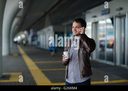 Close up portrait of a serious young man talking on mobile phone near the airport terminal with coffee Stock Photo
