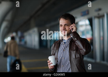 Close up portrait of a serious young man talking on mobile phone near the airport terminal with coffee Stock Photo