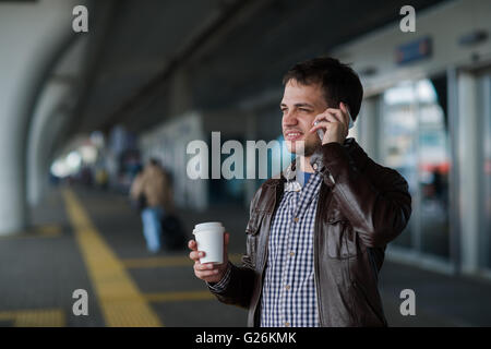 Man Using Mobile Phone near the airport terminal with a cup of coffee waiting for the taxi Stock Photo