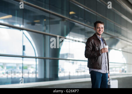 Young handsome man with coffee cup and suitcase in the airport Stock Photo