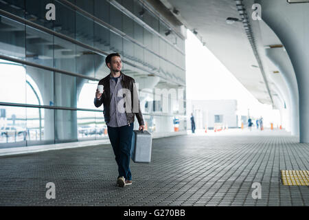 Full body portrait of a happy male traveler walking with bags and coffee Stock Photo