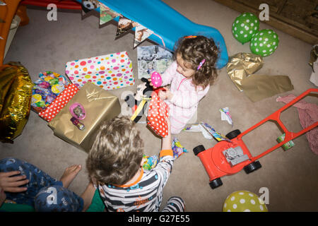Birthday morning two year old still in pajamas on floor of lounge tearing open gift wrappers surrounded by paper, mess and toys Stock Photo