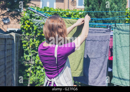A young woman is hanging her laundry on a clothes line in the garden on a sunny day Stock Photo