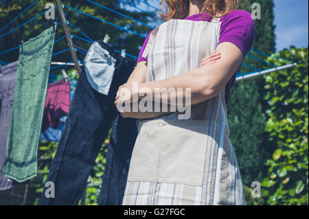 A young woman wearing an apron is standing by her laundry drying on a clothes line in the garden Stock Photo