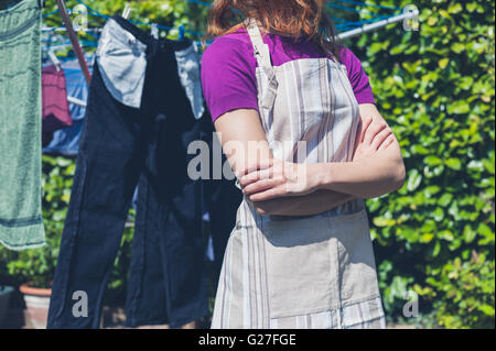 A young woman wearing an apron is standing by her laundry drying on a clothes line in the garden Stock Photo