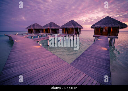 Over water bungalows with steps into amazing green lagoon with coral, Maldives sunset beach Stock Photo