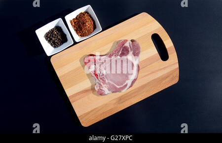 Meat steak on a cutting board and pepper, bay leaf, rosemary, onions, salt, olive oil, soy sauce on a black background Stock Photo