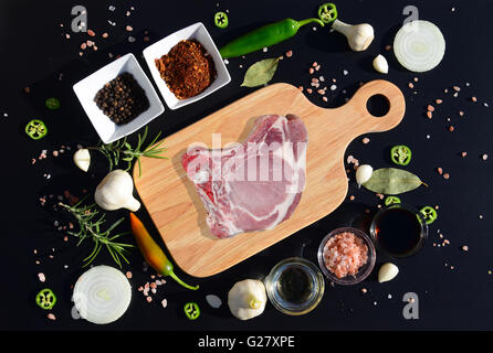 Meat steak on a cutting board and pepper, bay leaf, rosemary, onions, salt, olive oil, soy sauce on a black background Stock Photo