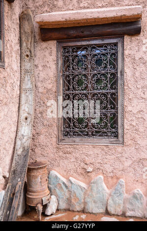 an ornate metal wrought iron grill on a closed Moroccan window in a terracotta coloured wall with a heavy lintel and stone skirting, Morocco Stock Photo