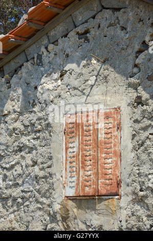 old rusty metal shutters with cut out flying bird shape vents closed on a rough cement concrete render wall with exposed fascia and roof tiles, Turkey Stock Photo