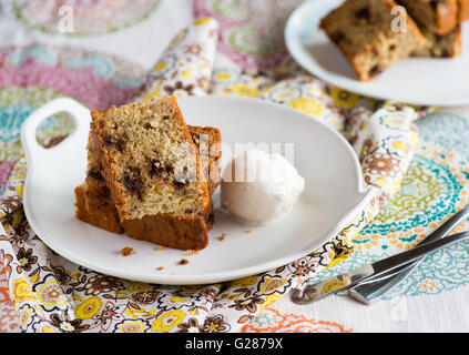 Homemade banana cake with chocolate chips, served with ice cream on white plate. Selective focus Stock Photo
