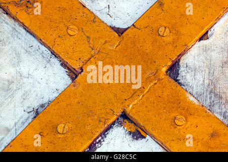 Close up of Rustic Yellow metal cross screwed onto grungy white painted panel Stock Photo