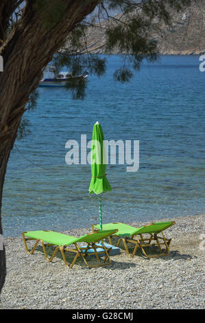 Two empty lime green sun loungers with a closed parasol sun shade on a shingle beach by the water's edge Stock Photo