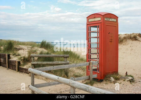 An old red telephone box stands among dunes on the edge of a sandy beach with a lone walker under a cloudy sky, UK Stock Photo