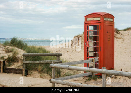 An old red telephone box stands among dunes on the edge of an empty sandy beach under a cloudy sky, UK Stock Photo