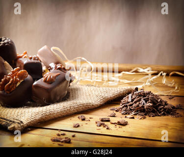 Group of bonbons stacked on a wood table close up. Black and white chocolate with nuts and straw decoration . Front view. Stock Photo